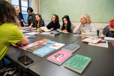 Na stole leżą książki z kolorowymi okładkami. Przy stole siedzą uczestniczki warsztatów.