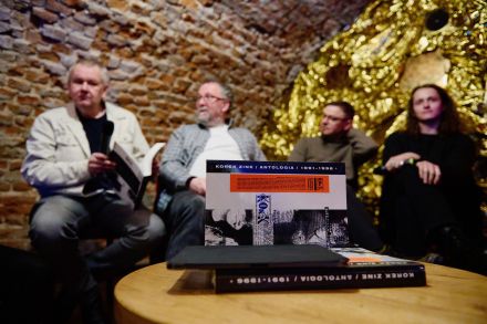 Przy stoliku siedzi czterech mężczyzn. Przed nimi leżą książki.