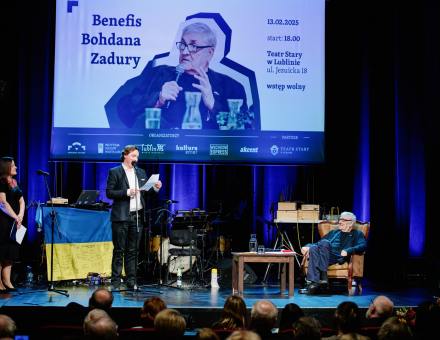 Młody mężczyzna czyta coś z kartki na scenie. Jubilat bardzo się uśmiecha.