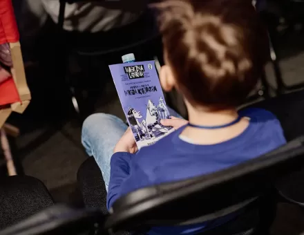 Chłopiec trzyma na kolanach gazetkę Magicznej Latarni.