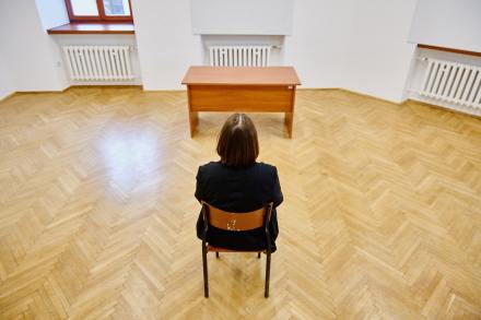 Na krześle siedzi kobieta. Widzimy ją tyłem.  Przed nią stoi biurko.