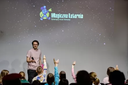 Mężczyzna zadaje pytanie dzieciom. Maluchy podnoszą ręce do góry. 