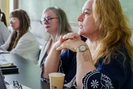 Uczestniczki spotkania siedzą przy stole i słuchają. 