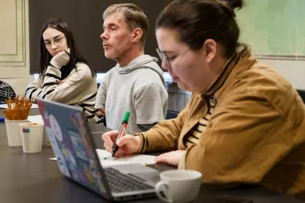 Przy stole siedzą dwie kobiety i mężczyzna. Jedna z kobiet obsługuje komputer.