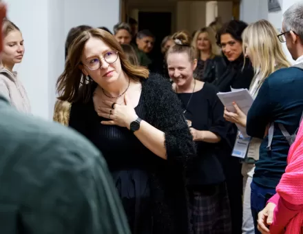 Tłum ludzi stoi na korytarzu przed wejściem do sali. Wśród nich są kuratorka wystawy i artystka.