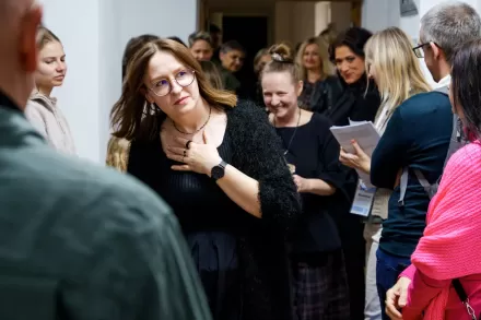 Tłum ludzi stoi na korytarzu przed wejściem do sali. Wśród nich są kuratorka wystawy i artystka.