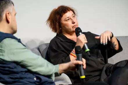 Kobieta siedząca na kanapie przy stoliku mówi do mikrofonu. 