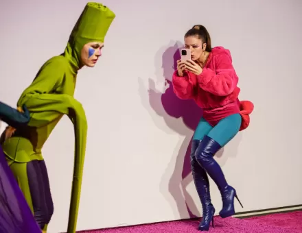 Jedna z aktorek przytula się do ściany i robi zdjęcie telefonem.