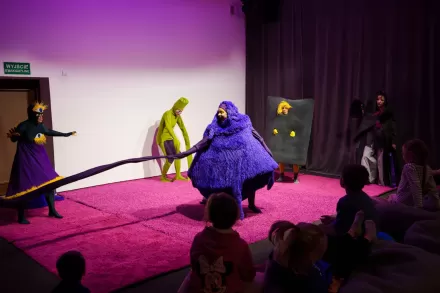 Aktorzy przebrani w stroje potworów biegają po różowym dywanie.