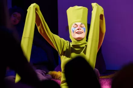 Zbliżenie na aktorkę, która ma zielony kostium z za długimi rękawami.