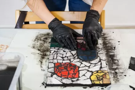 Dłonie w rękawiczkach wykańczają mozaikę.