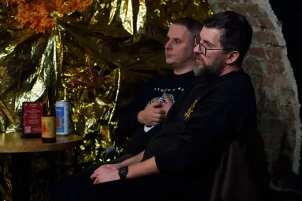 Dwaj mężczyźni siedzą przy stoliku i słuchają dyskusji.