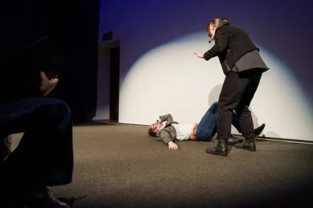 Mężczyzna upada na podłogę, kobieta chce mu pomóc wstać.