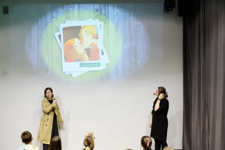 Na ścianie jest wyświetlony slajd z mamą, która przytula córkę. Prowadzące wskazują na ten obrazek.