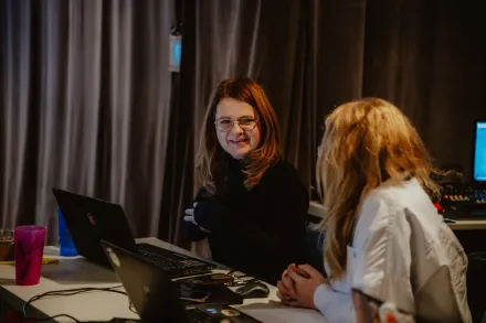 Dwie uczestniczki siedzą przy stole przy komputerach i uśmiechają się do siebie.