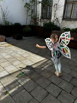 Dziewczynka ma na ramionach skrzydła motyla. Na ziemi odbijają się kolory z witrażu, który robiła.