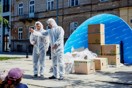 Dwaj mężczyźni odgrywają scenkę na ulicy. Są przebrani w białe kombinezony. 