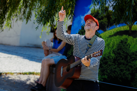 Artysta gra na gitarze i unosi jedną rękę do góry.