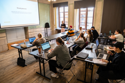 Uczestniczki warsztatów siedzą przy stołach. Przed nimi stoją laptopy.