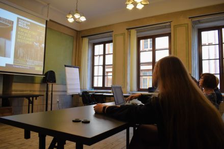 Dziewczyna siedzi przy laptopie i patrzy na wyświetlaną na rzutniku prezentację.