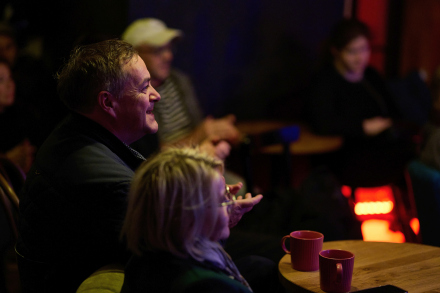 Kobieta i mężczyzna siedzą przy stoliku i biją brawo. Są uśmiechnięci.