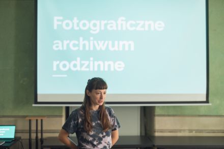 Kobieta stoi przed rzutnikiem, na którym wyświetla się napis "Fotograficzne archiwum rodzinne".