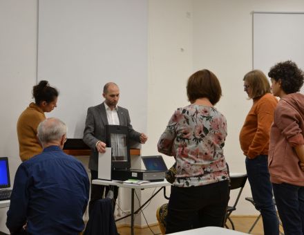 Uczestnicy spotkania stoją dookoła mężczyzny, który na skanerze prześwietla zdjęcie.