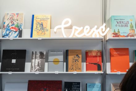 Zdjęcie dwóch regałów z ustawionymi książkami oraz świecącym napisem ,,Cześć".