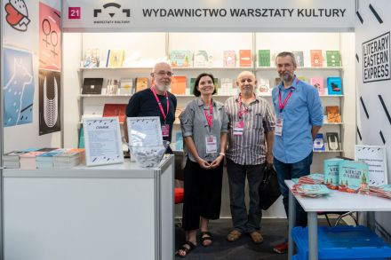 Zdjęcie osób reprezentujących stoisko ,,Wydawnictwo Warsztaty Kultury", stojących na tle regałów z książkami.