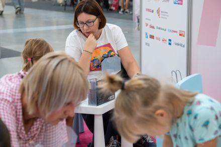 Dwie matki z córkami siedzą przy małych stolikach dla dzieci.