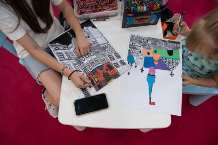 Zdjęcie zrobione z góry, przedstawiające kolorowanki z budynkami Lublina, kolorowane przez dwie dziewczynki.