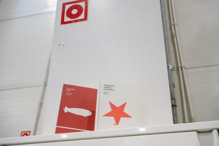 Zdjęcie dwóch, czerwono-białych książek o wojnie na Ukrainie, zrobione na tle białej ściany z czerwono-białą naklejką w rogu. 