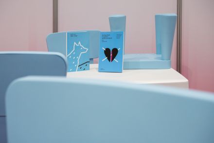 Dwie książki z niebieskimi okładkami, z wilkiem i sercem, stoją na białym stoliku i otoczone są niebieskimi krzesełkami.