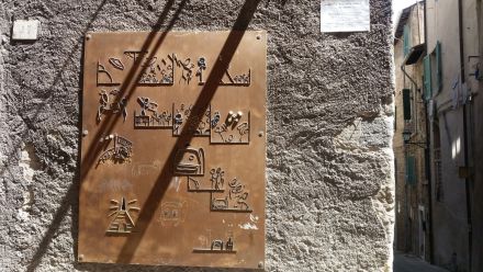 Na miedzianej blaszce, zawieszonej na ścianie budynku, widnieją małe powyginane blaszki ułożone w historyjki na wzór hieroglifów. egipskich. 