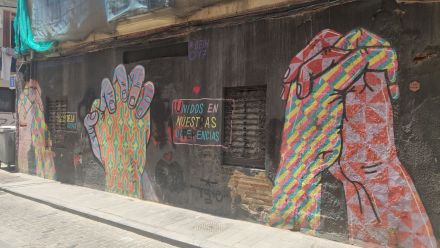 Mural przedstawia trzy pary trzymających się, kolorowych, wzorzystych dłoni na czarnym tle.