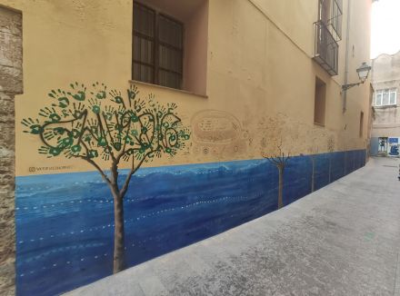 Budynek na dole ma namalowany niebieski pas, na którym widnieją drzewa. Pierwsze drzewo ma odbite ręce, które tworzą liście. Następne drzewa  za korony drzew  mają różne napisy.