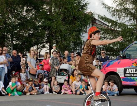 Plenerowy pokaz sztuki cyrkowej, na pierwszym planie artysta jadący na monocyklu,  w tle zgromadzona publiczność. Plenerowy pokaz sztuki cyrkowej, na pierwszym planie artysta jadący na monocyklu,  w tle zgromadzona publiczność.