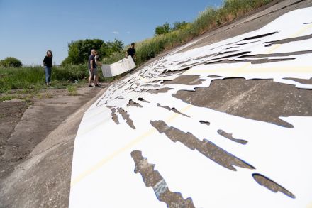 Zdjęcie zrobione z bocznej perspektywy przedstawia ułożony na zboczu biały szablon oraz kilka osób, które w oddali układają kolejny jego element. 