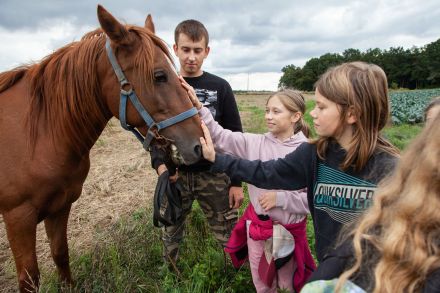 Dzieci głaszczą konia, którego trzyma młody mężczyzna.