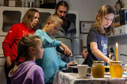 Chłopiec wlewa ciecz do pojemnika. Pozostałe dzieci przyglądają się mu. Na stole stoją miód i świeczki.