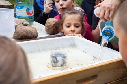 Pszczelarz wlewa wodę do najwyższej warstwy ula. Dzieci przyglądają się reakcji pszczół.
