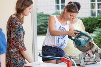 Plenerowy warsztat w ramach lekcji sztuki. Na zdjęciu widać trzy kobiety, jedna z nich pracuje przy użyciu piły tarczowej, pozostałe się przyglądają.