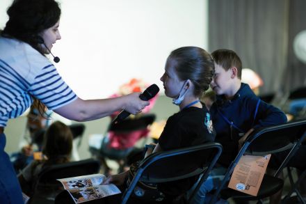Prowadząca trzyma mikrofon przy ustach dziewczynki.