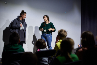 Klub filmowy dla najmłodszych w ramach Magicznej Latarni. Na zdjęciu widzimy prowadzącą oraz drugą towarzyszącą jej kobietę. Odgrywają one scenkę teatralną poprzedzającą seans.