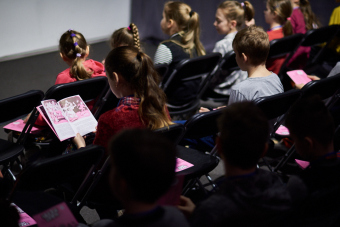 Klub filmowy dla najmłodszych w ramach Magicznej Latarni. Zdjęcie ukazuje dzieci na widowni, jedna dziewczynka przegląda komiks.