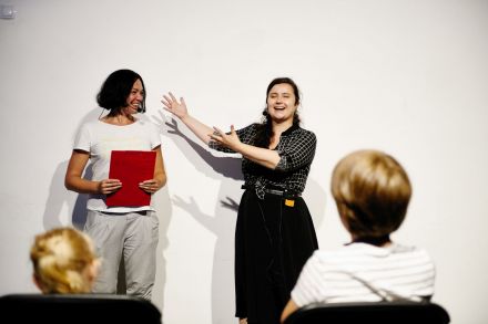 Jedna animatorka wskazuje na drugą, która trzyma w ręce książkę.