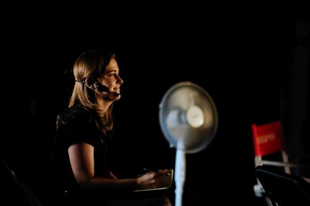 Zbliżenie na kobietę z mikrofonem w ciemnym pomieszczeniu.