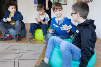 Zdjęcie ukazuje czterech chłopców, konsultujących się w parach. Trzymają w rękach karteczki. Na jednej z nich widnieje napis- ratusz.