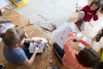 Zbliżenie na trzy dziewczynki, które wycinają i rozrysowują budynki, obiekty.