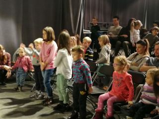 Zdjęcie przedstawiające publiczność teatru pacynkowego. Widzimy poruszenie wstających z miejsca dzieci.